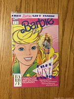 Front view of sealed Barbie Issue 1 comic showing cover art and attached miniature figurine