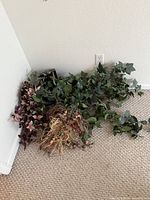 Pile of assorted artificial plants on carpet against wall