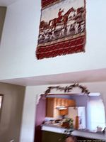 Full view of tapestry hanging high on wall showing fox hunting scene and red plaid border