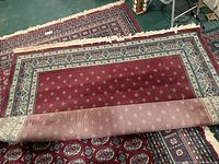 Full view of rolled red Persian-style rug with border and fringe