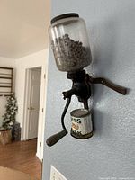 Full view of wall-mounted coffee grinder with glass hopper and catch cup