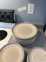 Stack of eight matching Pfaltzgraff dinner plates beside stove