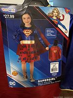 Retail packaging showing model wearing Supergirl costume, price, branding, size info