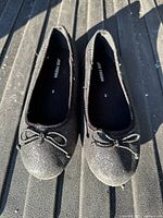 Top view of pair of black glitter ballet flats showing bow detail and size markings