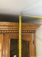 Top of oak corner cabinet showing crown moulding and tape measure indicating 83-inch height