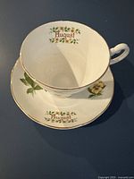 Teacup on saucer showing interior "August" text and floral motif