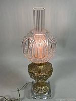 Full view lit lamp showing crystal globe, chimney, brass and crystal base