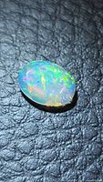 Oval opal showing multicolored flash on leather-like surface