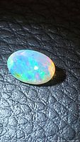 Oval faceted Ethiopian opal on black textured surface showing blue, green and orange play-of-color