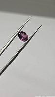 Front view of oval pink-purple spinel held in tweezers