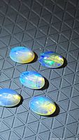 Five oval opals showing blue and green play of color on textured black surface