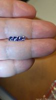 Three cushion cut deep blue tanzanite gemstones on fingertip