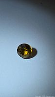 Front view of single round yellowish-green faceted gemstone