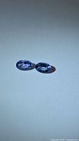 Two oval bluish-violet tanzanite gemstones on a white background