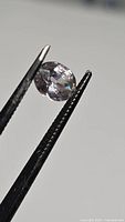 Oval spinel held by tweezers, side angle showcases color and inclusions