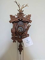 Front view of carved cuckoo clock showing dial, carvings, chains, and weights