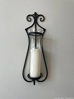 Front view of single wall sconce showing metal frame, glass hurricane and candle