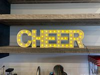 Front view of illuminated CHEER marquee sign on shelf