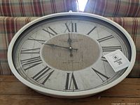 Front view of white oval wall clock showing dial and frame