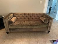 Front view of sage green tufted velvet couch with two cylindrical bolsters