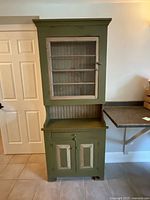 Full view of vintage green wooden display cabinet showing upper glazed section and lower cupboard