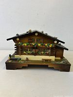 Front view of carved wood Swiss chalet music box showing windows, shutters, flower boxes and base
