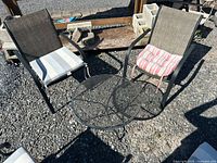 Set overview: two chairs with cushions and round mesh table on gravel
