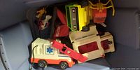 Bin containing multiple Fisher-Price vehicles including ambulance, tow truck, helicopter and service truck