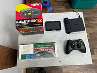 All five items arranged on table: radar detector boxed, GPS, Fire TV, remote, Xbox controller, birdbath heater boxed