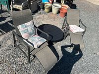 Wide view of two sling lounge chairs, side table, and cushions on gravel surface
