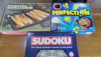 Overall view of three boxed games: Tournament Backgammon, Perfection, Sudoku