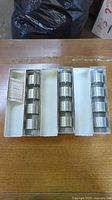 All three slim boxes open showing twelve pewter napkin rings and small information card