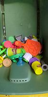 Mixed Play-Doh accessories in green bin including tubs, orange mold tray, various tools