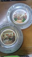 Both pewter-rimmed commemorative plates showing different center images