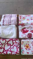 Six towels laid out showing heart rows, cupcake print, plain white, mug print, outlined hearts, radial burst heart