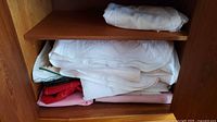 Stack of folded white quilt-stitched tablecloths with pink, red and green pieces beneath on shelf