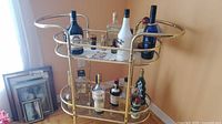 Full view of bar cart with bottles for scale, shows gold frame, glass shelves, casters