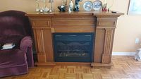 Full view of oak mantel electric fireplace beside chair