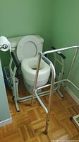 Raised toilet seat installed on toilet with safety frame and walker in view