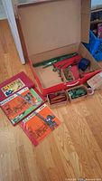Open Meccano box with assorted metal parts and manuals on floor