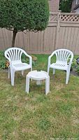 Two white plastic armchairs and matching round side table on lawn
