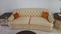 Front view of beige damask sofa with two orange pillows