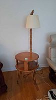 Full view of round two-tier wood side table with attached floor lamp and shade