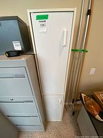 Front view of tall white cupboard beside other office furniture