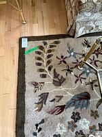 Corner of beige floral wool rug on hardwood floor showing dark brown border and pattern detail
