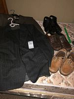 Charcoal pinstripe suit jacket, brown-grey jacket underneath, three pairs of shoes on mattress