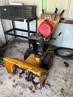 Front three-quarter view of snow blower with gas can mounted on handle