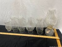 Lineup of oil lamp and five chimneys with ruler for scale