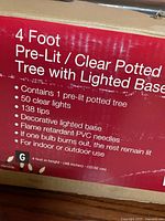 Box close-up showing product specifications: 4 ft, pre-lit, clear lights, 50 lights, 138 tips, flame-retardant PVC, indoor/outdoor