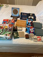 Overview of all games on bed including Jenga, Skip-Bo, Lego set, playing cards, dartboard, backgammon, peg board, Battleship boards